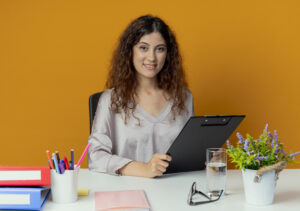 smiling young pretty female office worker sitting at desk with office tools holding clipboard isolated on orange background SSUCv3H4sIAAAAAAAACpyRy47DIAxF9yPNP0SsGyltQvr4lWoWDtAElUDFY0ajqv8+BkLFenb42L72Nc/Pj6YhEzjJyKV5xghjqVRw3oKXRiPudhu3QnNhayK49MZKUDWcwLNFwyoQ6qBUxK+UJM6DD064OGxDDLyYUSPDt0Te6JrjpiRSEjswRciuYi5MiRWUxf/VmR9fxQ3MQrPftHBlxAolIBu55lJy//HCrrU1CFyaytW3YaBiQV8pPaxkUs9Vm/FLunJpYyZob+MK782JMuYBk4onvqGmKHwB57CcF14NYvinZq3maOOTgU2VcPyJGO77wzCe6XAeu552I6WHrSD/3iJRJ61ThDBmd8lr6zJuQLruNJ2OlLeUjdAOgtEWjvTW7jkd+EBPfBp6PPzrDwAA//8DAB9MfUuHAgAA